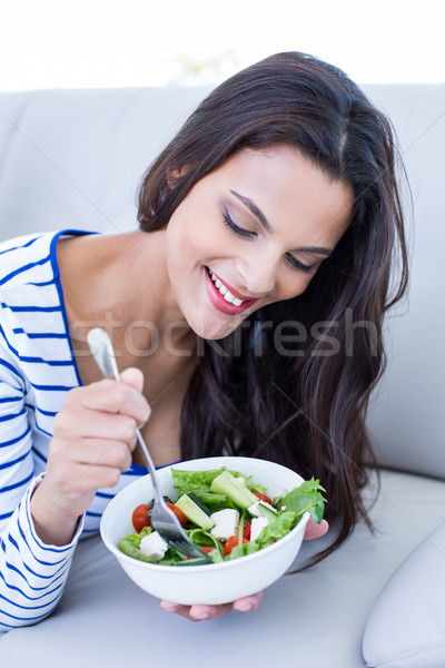 Smiling beautiful brunette relaxing on the couch and eating sala Stock photo © wavebreak_media