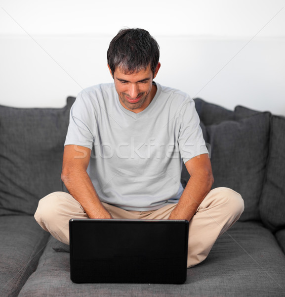 Bright man using a laptop on a grey sofa Stock photo © wavebreak_media