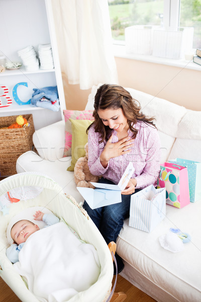 Bright woman sitting on the sofa with bags reading a card while her baby is sleeping in his cradle a Stock photo © wavebreak_media