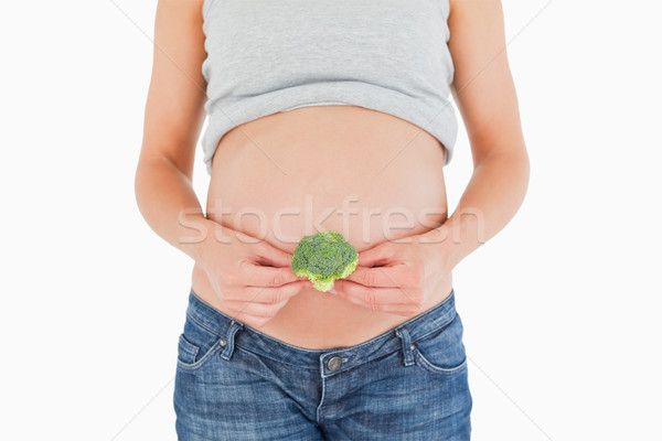 Stock photo: Young pregnant woman holding a broccoli while standing against a white background