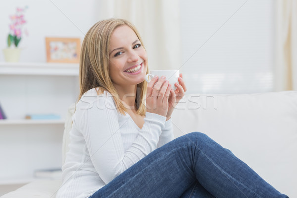 Stock photo: Smiling woman with coffee cup sitting on couch