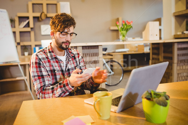 Stock photo: Graphic designer text messaging on mobile phone with laptop on t