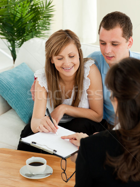 Bright young couple signing a contract sitting in their living room with a saleswoman Stock photo © wavebreak_media
