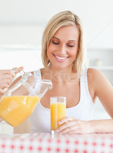 Close up of a smiling woman sitting at a kitchentable filling orange juice in a glass smiling Stock photo © wavebreak_media