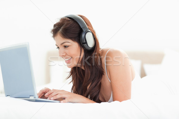 Stock foto: Frau · Bett · mit · Laptop · hören · Kopfhörer · lächelnde · Frau