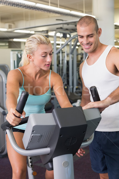 Trainer assisting woman with exercise bike at gym Stock photo © wavebreak_media