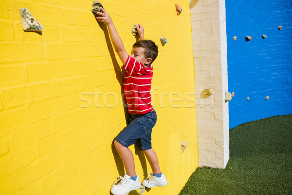 Portrait of smiling boy climbing yellow wall at playground Stock photo © wavebreak_media