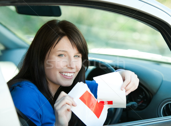 Stock photo: Charming brunette teen girl sitting in her car tearing a L-sign