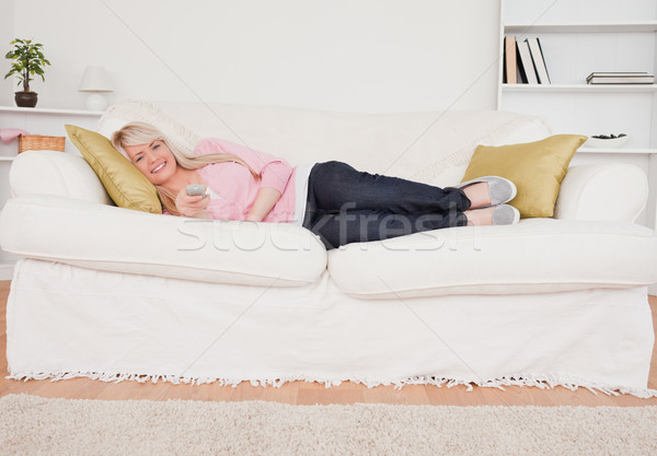 Attractive blonde woman watching tv while lying on a sofa in the living room Stock photo © wavebreak_media