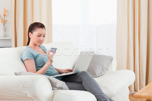 Stock photo: Lovely woman making an online payment with her credit card while sitting on a sofa in the living roo