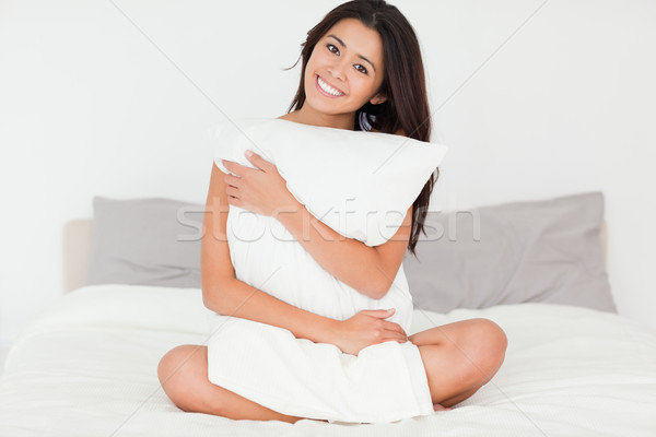 Stock photo: brunette woman with pillow sitting on her bed looking into camera in bedroom