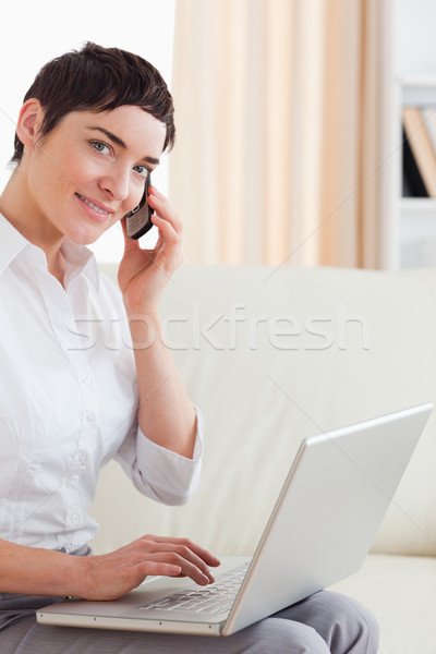 Short-haired woman with a laptop and a phone looking into the camera in the living room Stock photo © wavebreak_media