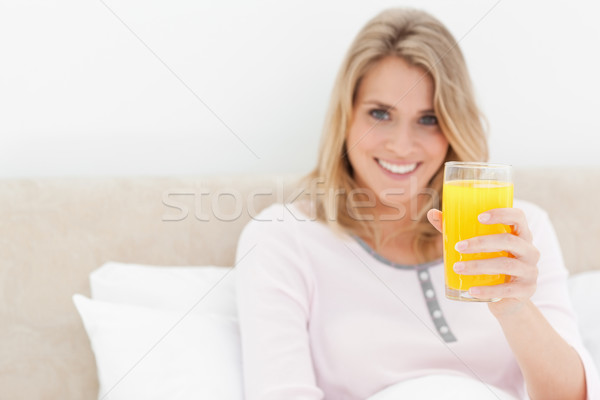 A woman holding a glass of orange juice while smiling and looking forward, while in bed. Stock photo © wavebreak_media