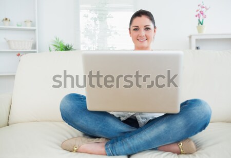 Woman sitting cross-legged on a couch in a living room and using a laptop Stock photo © wavebreak_media