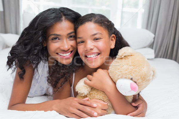 Stock photo: Pretty woman lying on bed with her daughter smiling at camera