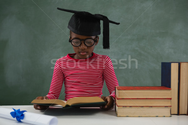 Schoolgirl in mortar board reading book against chalkboard Stock photo © wavebreak_media