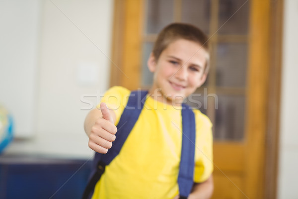 Smiling pupil with schoolbag doing thumbs up in a classroom Stock photo © wavebreak_media