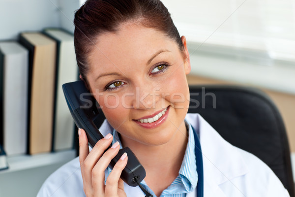 Attractive female doctor phoning in her office sitting at her desk Stock photo © wavebreak_media