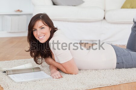 Stock photo: Young charming female reading a magazine while lying on a carpet in the living room