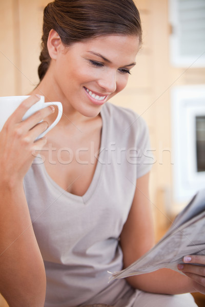 Stock photo: Smiling young woman reading newspaper while having tea