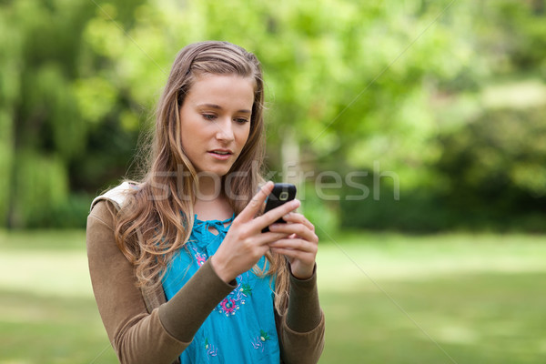 Serious teenager sending a text with her cellphone while standing in a park Stock photo © wavebreak_media