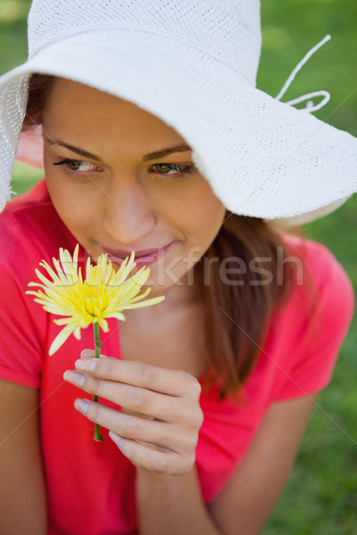 Woman wearing a white hat while smelling a yellow flower while looking towards the side, with grass  Stock photo © wavebreak_media