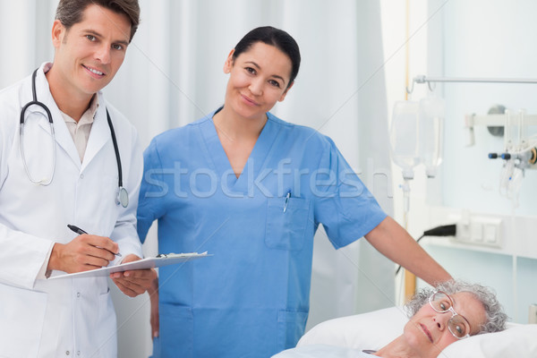 Doctor and nurse looking at camera next to a patient lying in hospital ward Stock photo © wavebreak_media