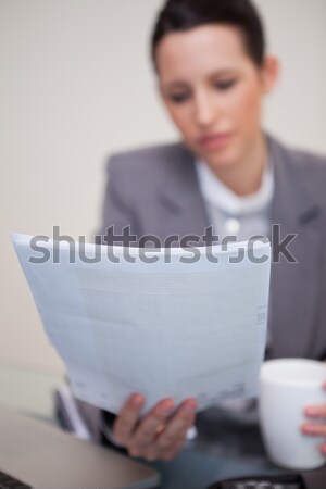 Stock photo: Business woman with coffee cup and laptop reading paper at offic