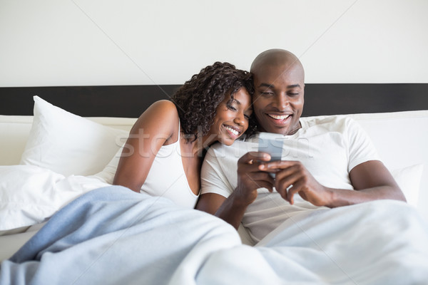 Happy couple cuddling in bed with smartphone Stock photo © wavebreak_media
