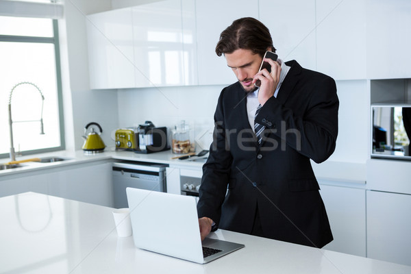 Affaires utilisant un ordinateur portable parler téléphone portable cuisine maison [[stock_photo]] © wavebreak_media