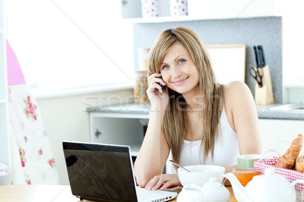 Caucasian woman using a laptop and a phone in the kitchen Stock photo © wavebreak_media