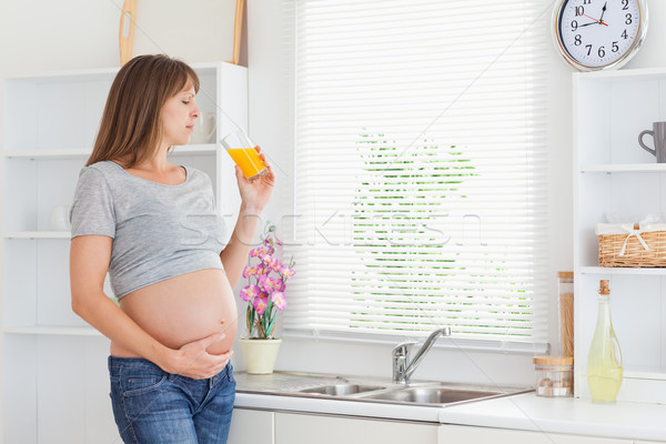 Beautiful pregnant woman drinking a glass of orange juice while standing in a kitchen Stock photo © wavebreak_media