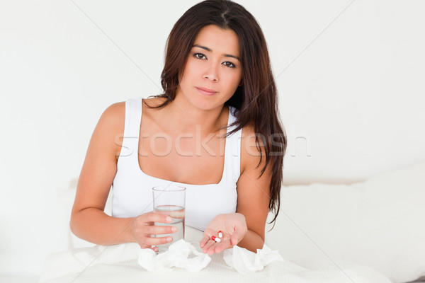 brunette woman having a cold sitting in bed taking pills looking into camera in bedroom Stock photo © wavebreak_media