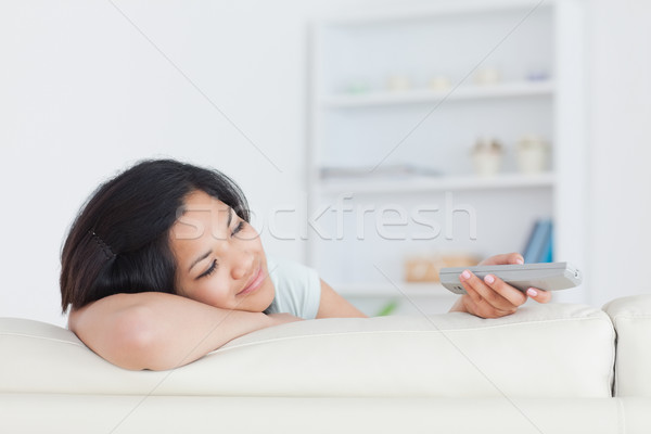 Smiling woman resting her head on her arm as she sits on a sofa and holds a remote in a living room Stock photo © wavebreak_media