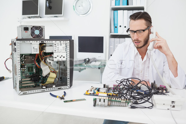Computer engineer looking at broken device and making a phone ca Stock photo © wavebreak_media