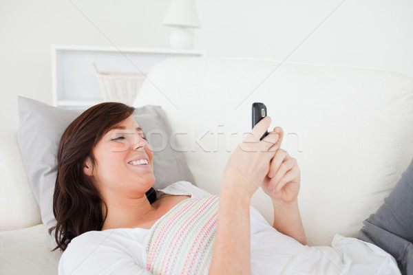 Good looking brunette female writing a text on her mobile while lying on a sofa in the living room Stock photo © wavebreak_media