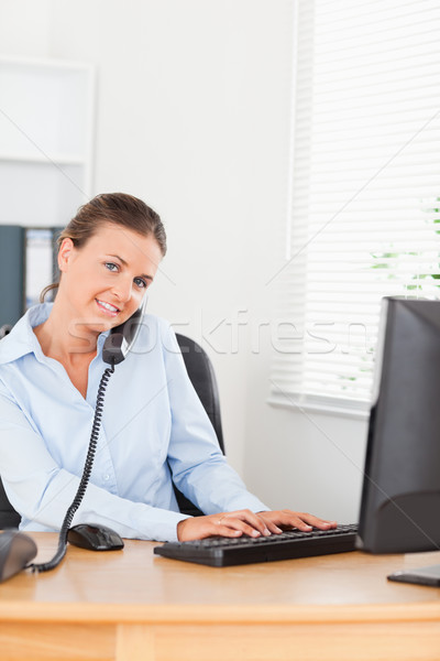 Secretary answering the phone while typing on her keyboard in her office Stock photo © wavebreak_media