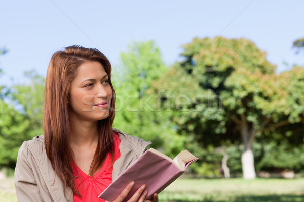 Young woman smirking towards the side while reading a book in a sunny grassland environment Stock photo © wavebreak_media