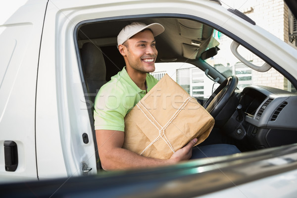 Stock photo: Smiling delivery driver in his van holding parcel