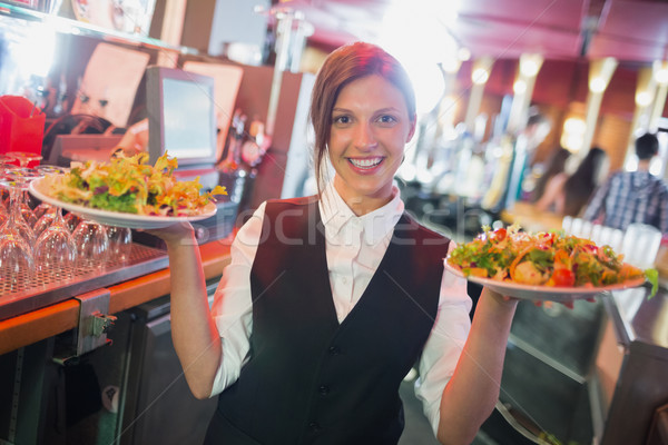 Pretty barmaid holding plates of salads Stock photo © wavebreak_media