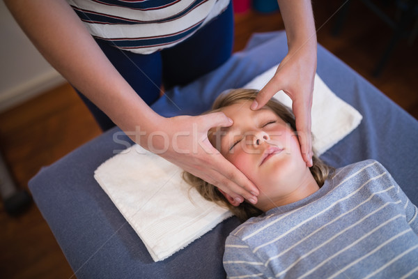 Stock photo: High angle view of boy with eyes closed receiving head massage from female physiotherapist