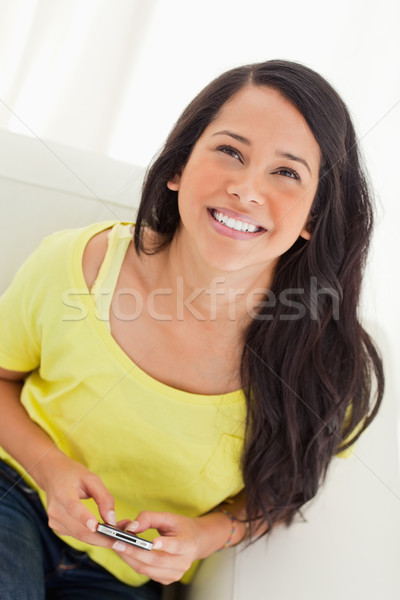 High-angle view of a happy Latino looking up while sitting on a sofa with her smartphone Stock photo © wavebreak_media