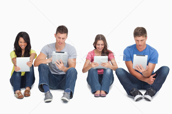 A group of four people sitting beside each other on the ground as they all use their tablet pc's Stock photo © wavebreak_media