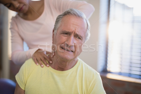 Senior male patient frowning while receiving neck massage from therapist Stock photo © wavebreak_media