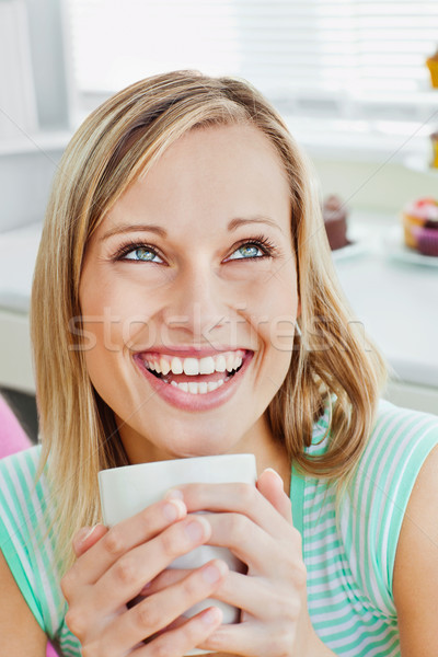 Stock photo: Laughing woman holding a cup of coffee at home in the kitchen