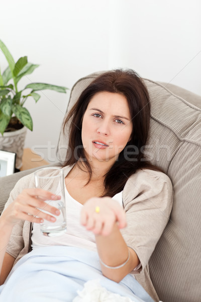 Sick woman showing a pill to the camera lying on the sofa Stock photo © wavebreak_media