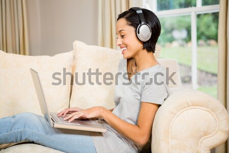 Stock photo: Beautiful red-haired woman listening to music with headphones while relaxing with her laptop in the 