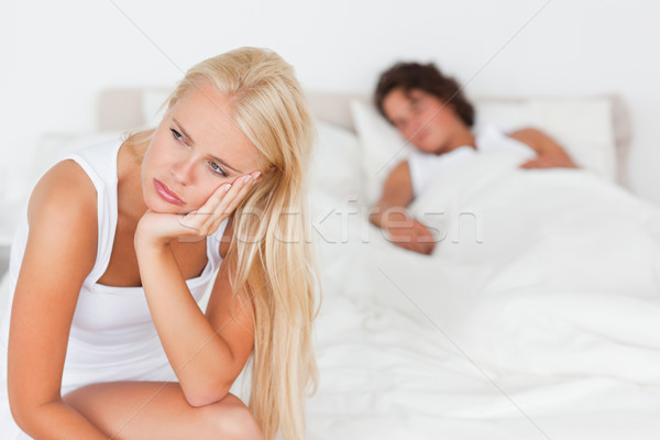 Upset woman sitting on a bed while her fiance is sleeping with the camera focus on her Stock photo © wavebreak_media