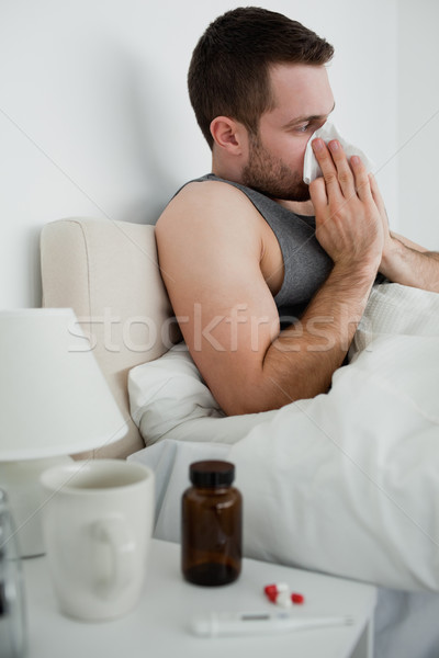 Stock photo: Portrait of a handsome man blowing his nose in his bedroom