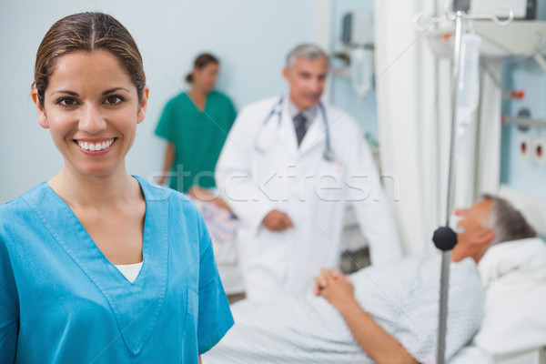 Happy nurse in hospital room with doctor, patient and other nurse in background Stock photo © wavebreak_media